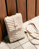 Candid shot of the white beaded mini bag resting against a wooden background, highlighting the natural jute materials and organic aesthetic.
