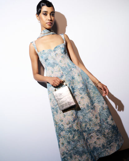 Model in a blue floral gown holding the Modern World silver metal bag, highlighting its artisanal character for formal event styling.