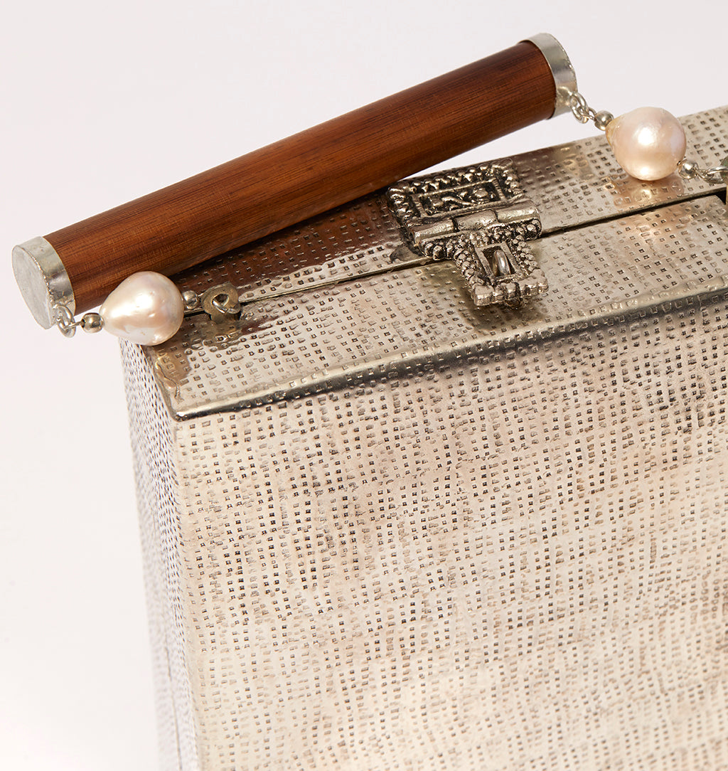 Detailed close-up of the dark wooden bar handle and shimmering pearl accents on the silver brass Modern World handbag.