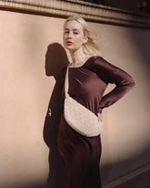 Model in a brown silk dress wearing the cream Moving Through bag as a crossbody, demonstrating its ergonomic fit and neutral shimmer