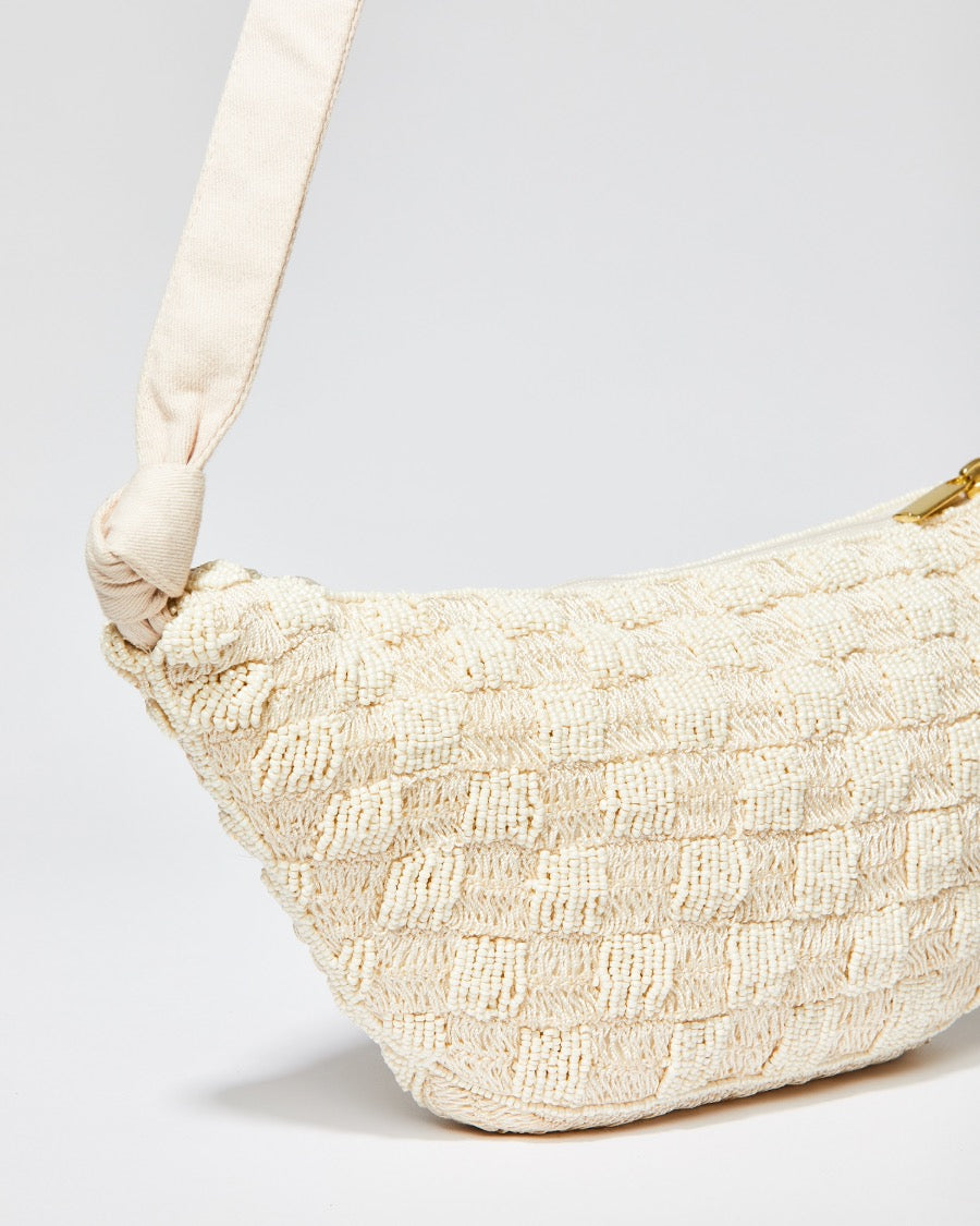 Side profile of the cream Moving Through bag emphasising the 35cm curved width and the secure gold zipper closure.