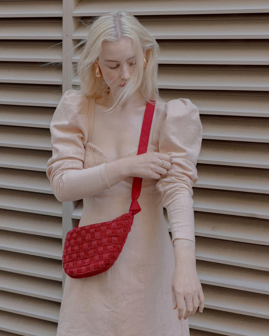 Model in a pale puff-sleeve dress wearing the red Moving Through bag as a crossbody, demonstrating its ergonomic fit and vibrant shimmer.