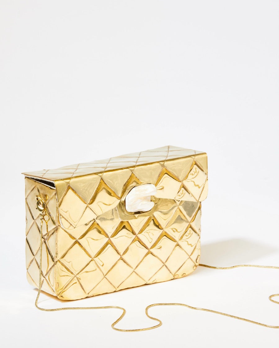 Three-quarter studio view of the gold Our Longing metal bag featuring a hand-beaten quilted texture and sculptural shell clasp.