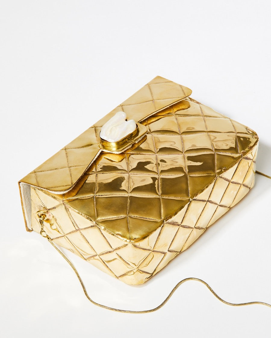 Angled view of the gold quilted metal clutch with its removable gold chain strap, demonstrating its versatility as a shoulder bag.