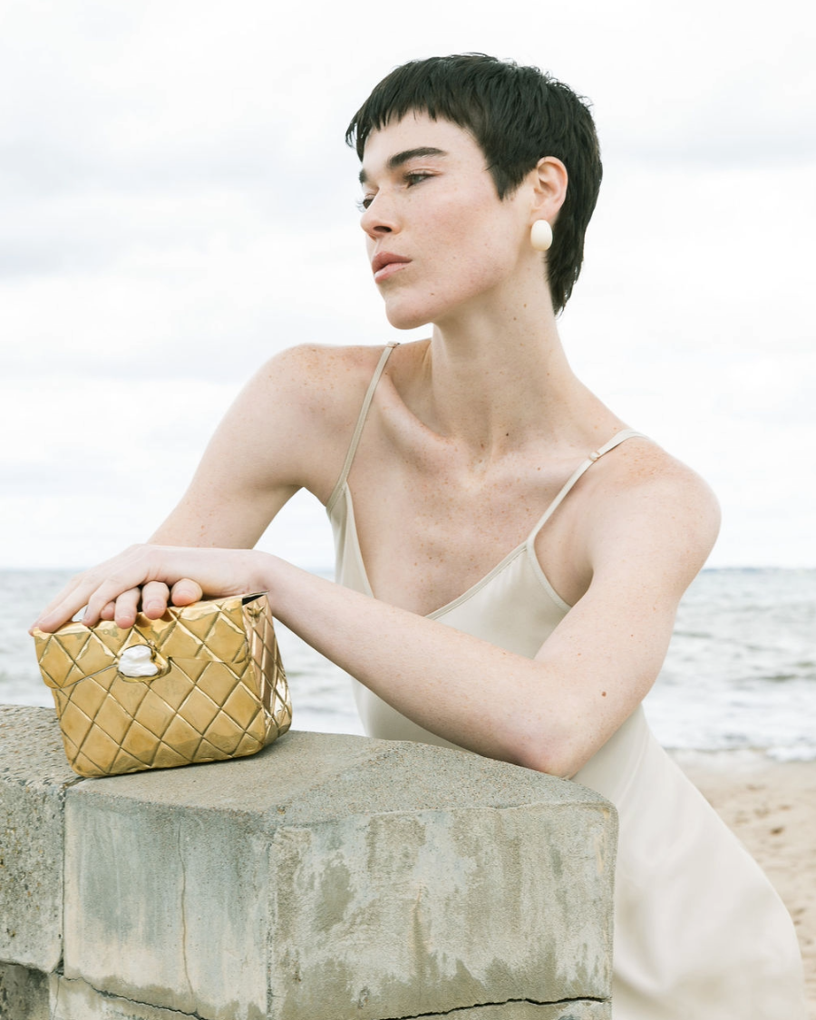 Close-up of a model holding the gold Our Longing bag, emphasising the unique character and craftsmanship of the hand-beaten brass.