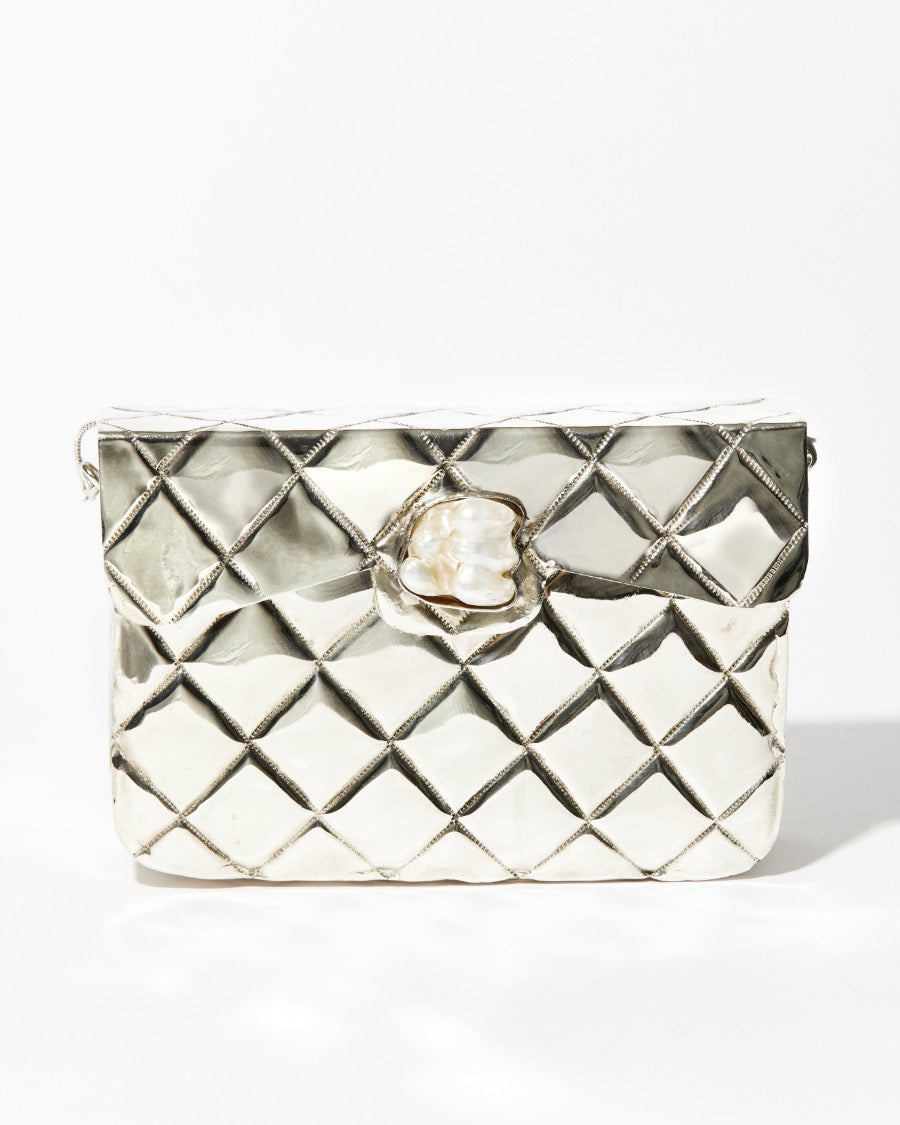Front studio view of the silver Our Longing metal bag featuring a hand-beaten quilted texture and a signature shell-shaped clasp.