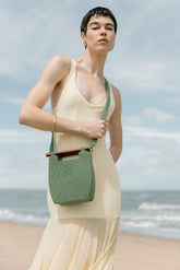 Model in a cream gown wearing the jade green Reach for Words bag as a crossbody, highlighting its vibrant hand-dyed glass beads.