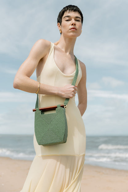 Model in a cream gown wearing the jade green Reach for Words bag as a crossbody, highlighting its vibrant hand-dyed glass beads.