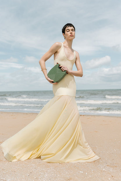 Full-length lifestyle shot of a model at the beach carrying the jade green beaded bag, showcasing its elegant scale and sculptural form.