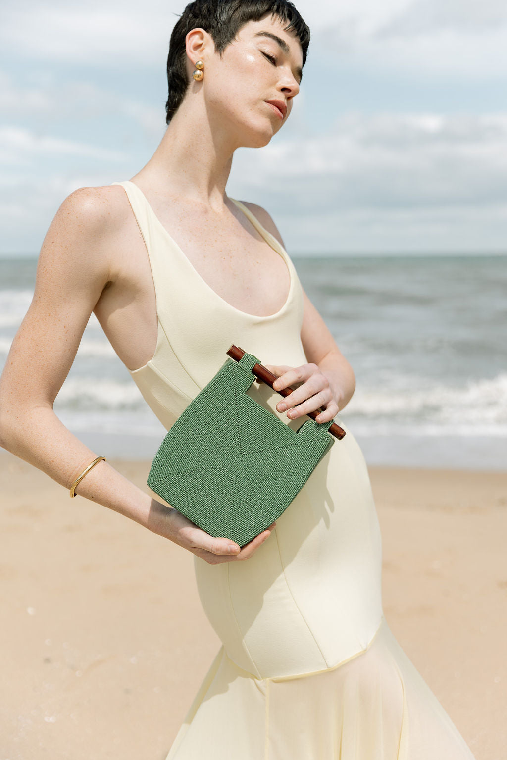 Close-up of a model holding the jade green beaded bag by its wooden bar handles, demonstrating its use as a statement top-handle bag or cross-shoulder bag.