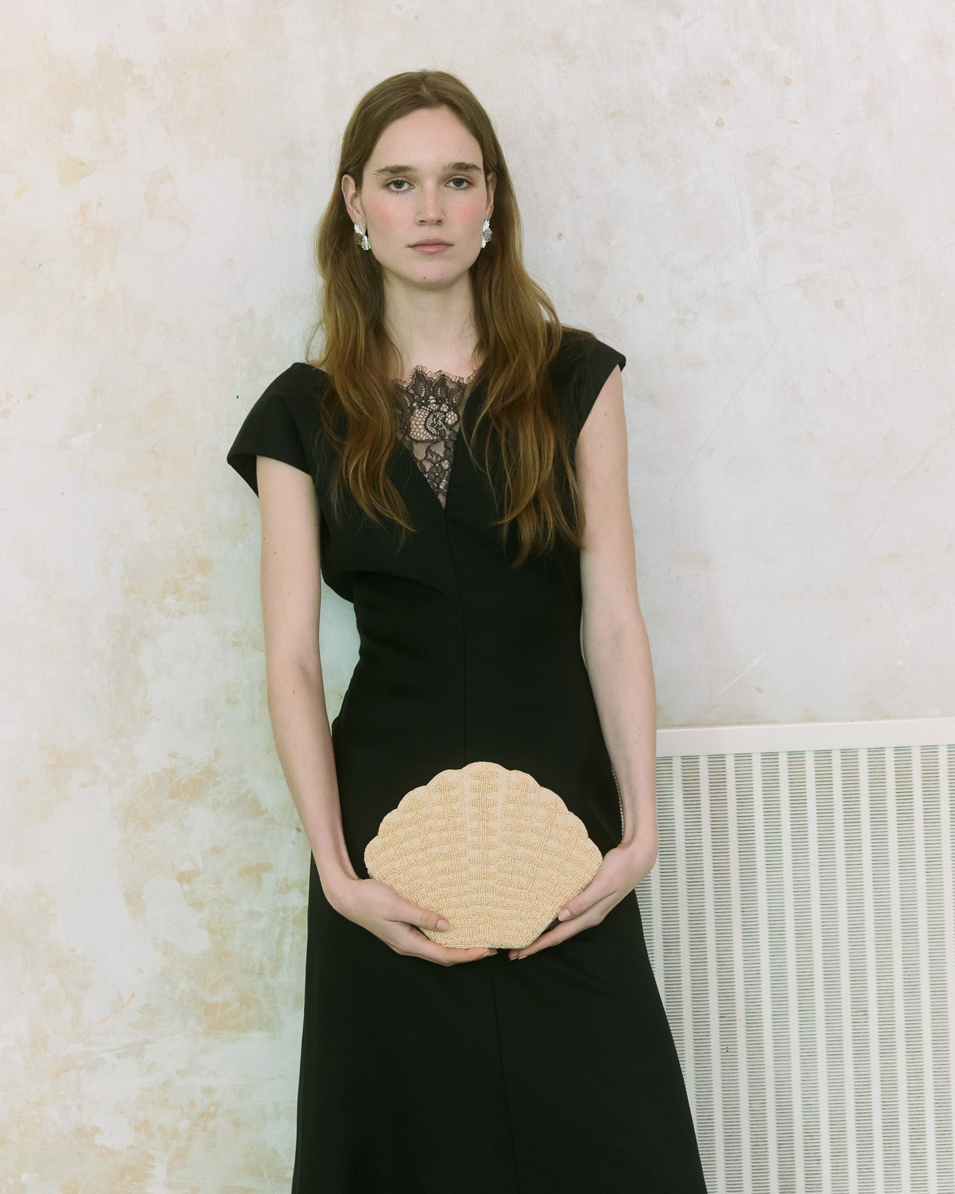 Model standing in black dress holding shell shaped beaded clutch bag by the hold 