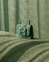 Artistic close-up of the jade green Uncovered Layers bag on a textured surface, highlighting the intricate hand-beaded woven construction.