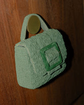 Close-up of the jade green beaded bag hanging against a wood background, showcasing the Melbourne-designed sculptural silhouette.