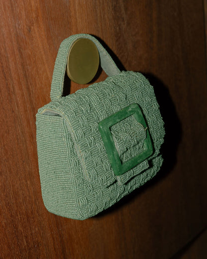 Close-up of the jade green beaded bag hanging against a wood background, showcasing the Melbourne-designed sculptural silhouette.