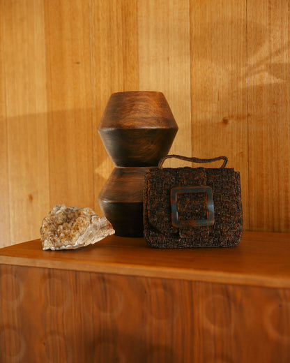 An artistic still life shot of the rich brown Uncovered Layers bag alongside a ceramic vase, emphasizing its sculptural design.