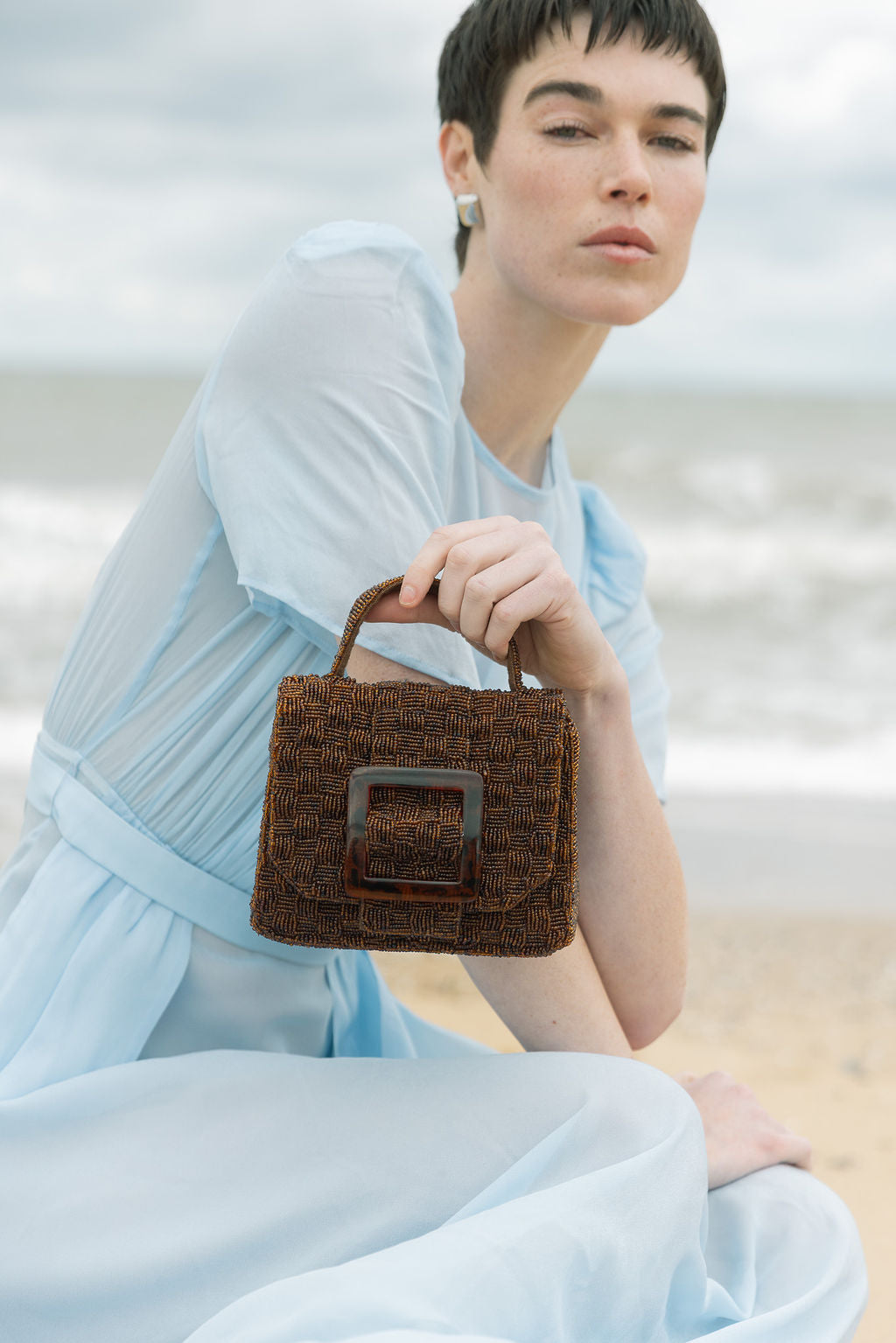 Model holding the brown beaded handbag by its top handle, demonstrating its transition from a day bag to a sculptural evening piece.