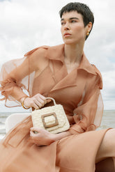 Close-up of a model holding the white Uncovered Layers bag by its beaded top handle, demonstrating its use as an elegant handheld evening bag.