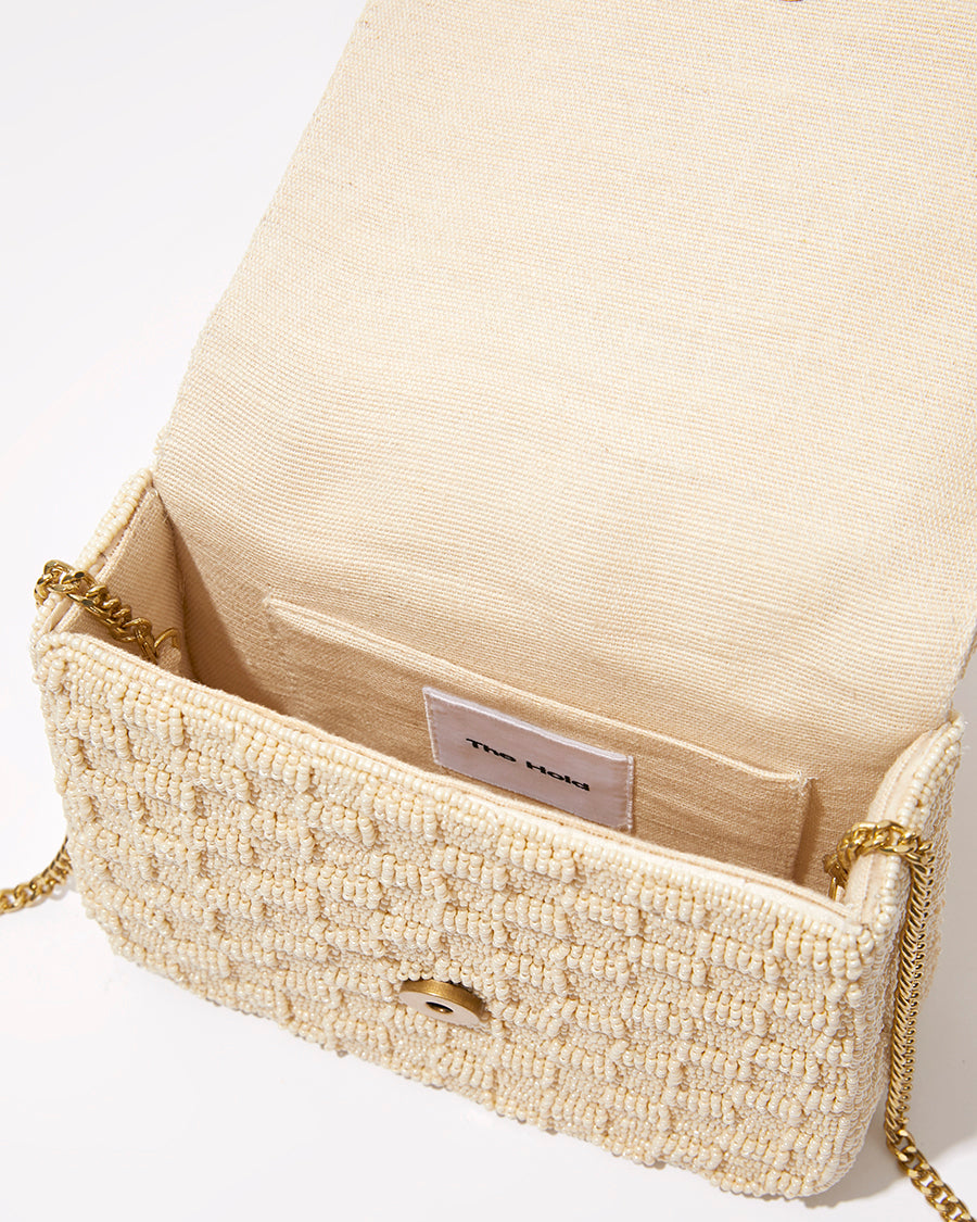 Open view of the white beaded bag showing the natural jute lining and internal space designed to fit an iPhone Plus and small essentials."