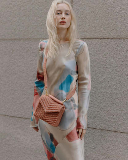 Model wearing a patterned dress styling the peach Waves Never Cease bag as a trendy crossbody accessory for outdoor events.