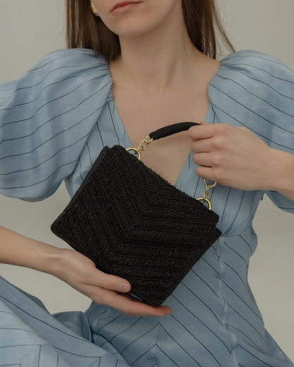 Model wearing a blue puff-sleeve dress holding the artisan-made black beaded handbag, demonstrating its size for evening essentials.