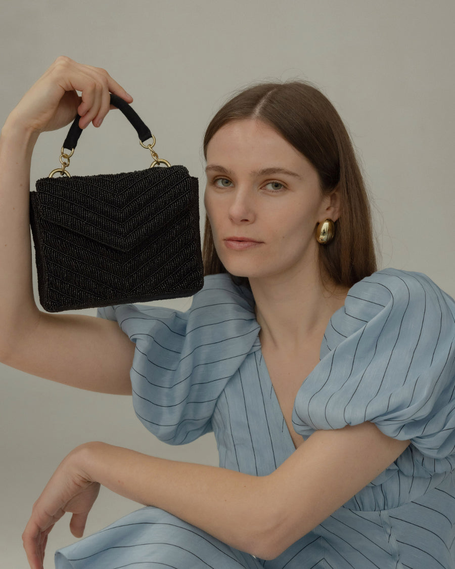 Model holding the Waves Never Cease bag by its jute top handle, showcasing a trendy and effortless elegance for formal events