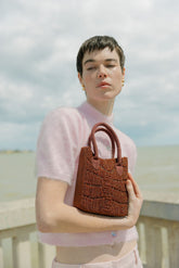 Model in a pink top holding the hand-beaded burgundy bag, an artisan-made burgundy beaded bag.