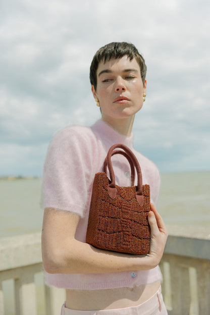 Model in a pink top holding the hand-beaded burgundy bag, an artisan-made burgundy beaded bag.