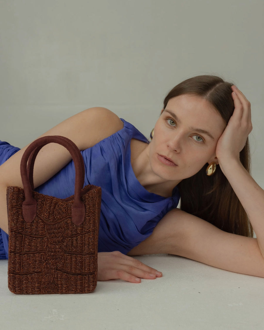 Close-up of a model with the artisan-made beaded bag, emphasising the intricate hand-crafted detail and dark cherry color.