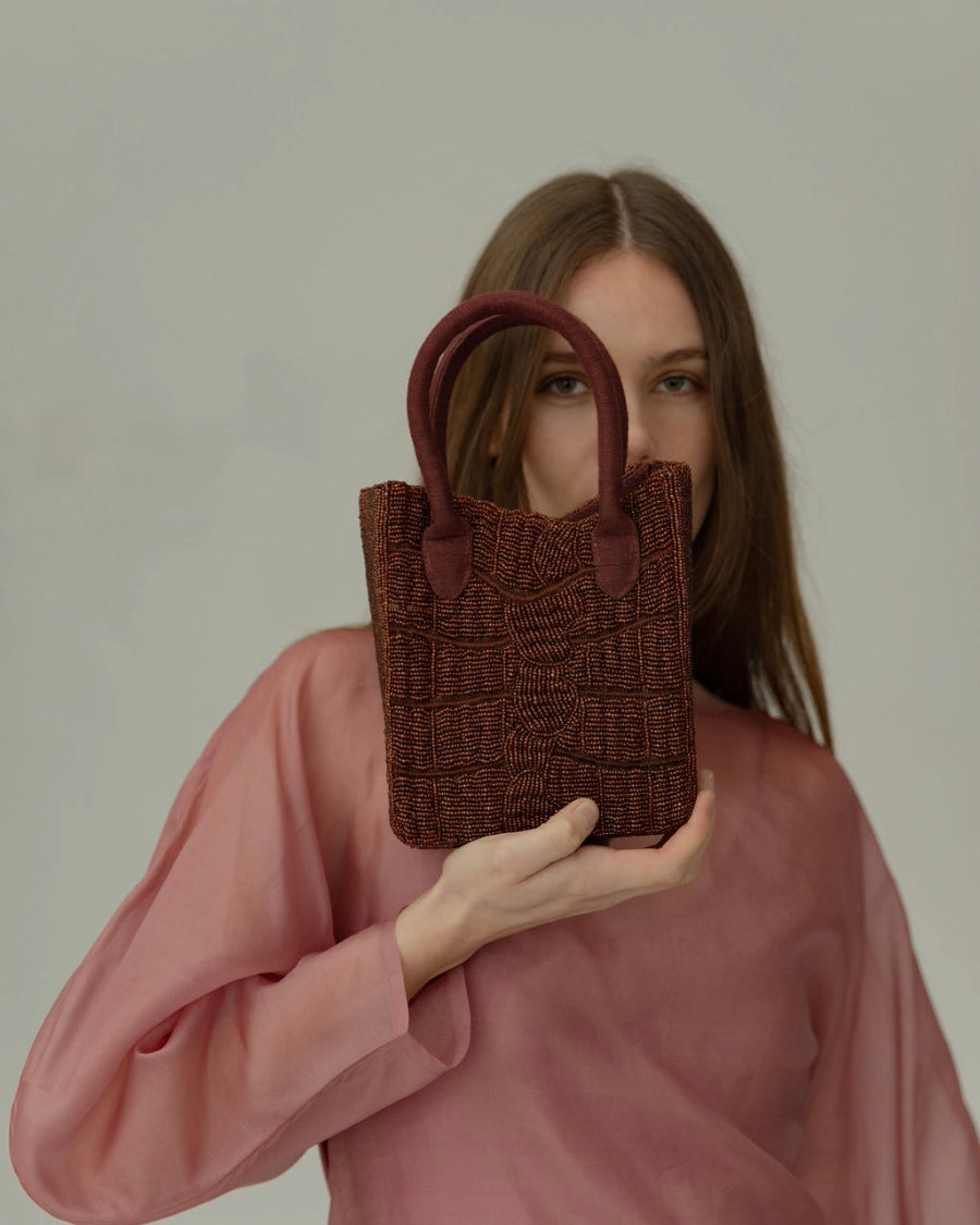 Model in a sheer pink dress holding the artisan-made burgundy bag, a trendy choice for weddings or evening events