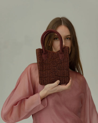 Model in a sheer pink dress holding the artisan-made burgundy bag, a trendy choice for weddings or evening events