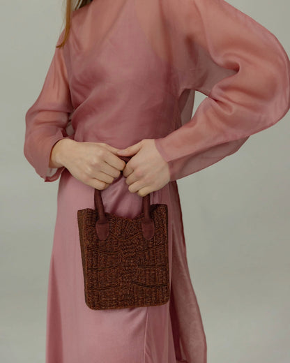 Close-up of a model with the artisan-made beaded bag, emphasising the intricate hand-crafted detail and dark cherry colour.