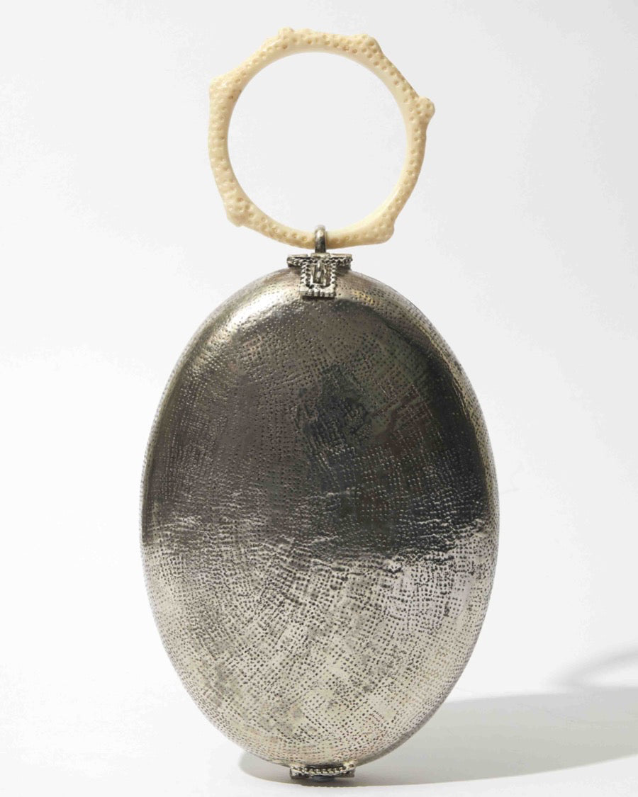 Front studio view of the Capacity for Presence silver metal bag, featuring an oval hand-beaten brass body and a cream coral-inspired resin handle.