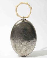 Front studio view of the Capacity for Presence silver metal bag, featuring an oval hand-beaten brass body and a cream coral-inspired resin handle.