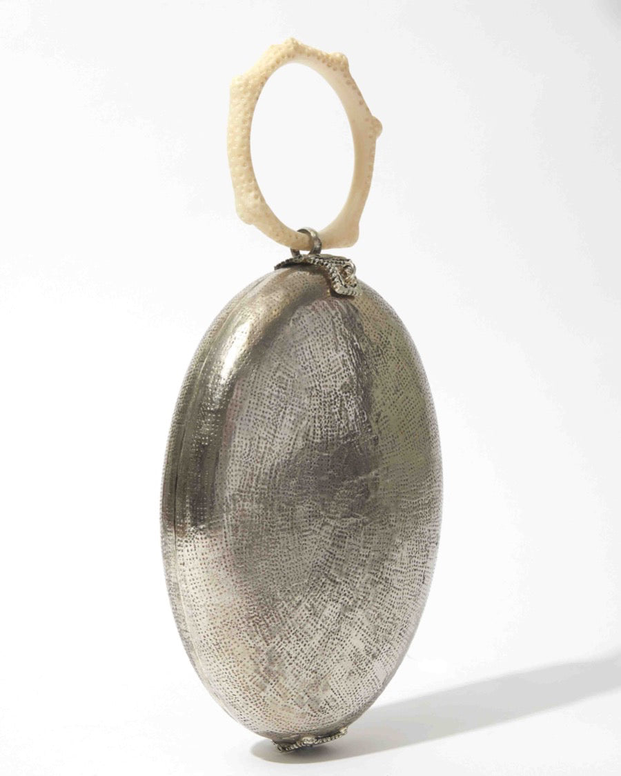 Side profile of the Capacity for Presence bag emphasising the contrast between the silver metal body and the sculptural hand-poured coral handle.