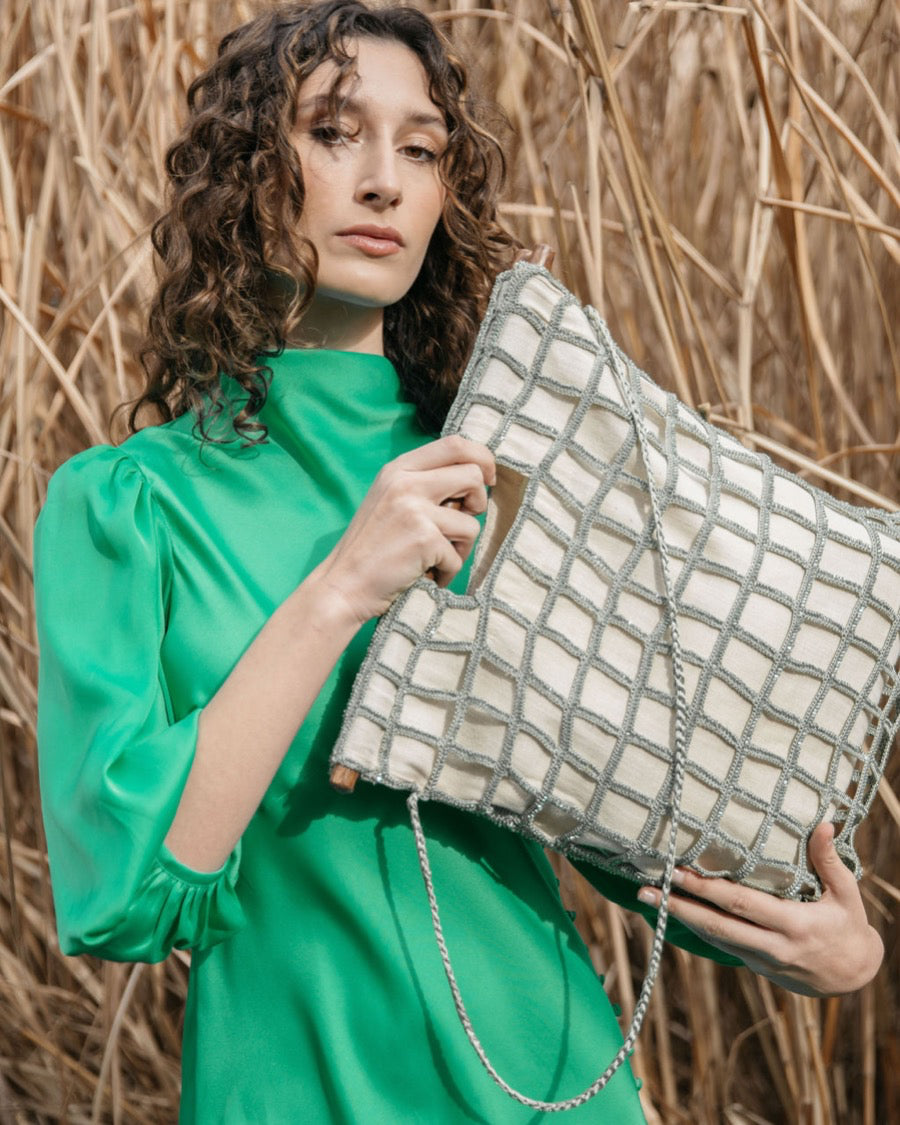 Model in a green silk dress holding the Entwined Tote, demonstrating its elegant hand-carried style and sculptural statement handles.