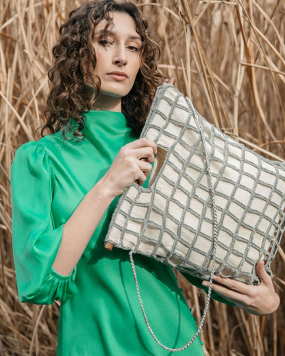 Model in a green silk dress holding the Entwined Tote, demonstrating its elegant hand-carried style and sculptural statement handles.