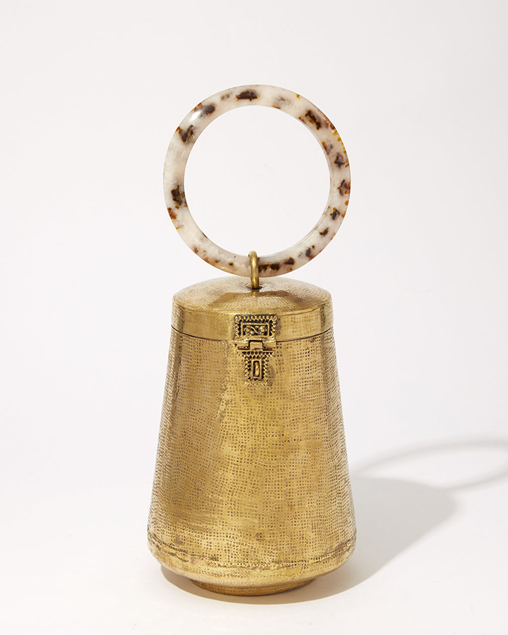 Front studio view of the Perception of Time gold brass bag, featuring a tapered hand-beaten metal body and a circular tortoiseshell resin handle.