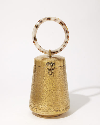 Front studio view of the Perception of Time gold brass bag, featuring a tapered hand-beaten metal body and a circular tortoiseshell resin handle.