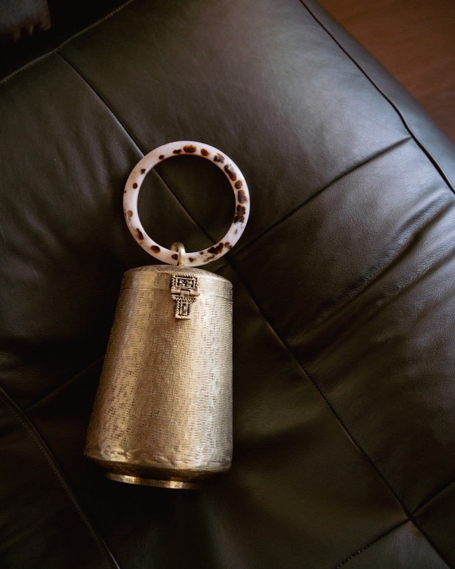 Still life shot of the Perception of Time gold bag on a black leather chair, highlighting the reflective properties of the hand-beaten brass.