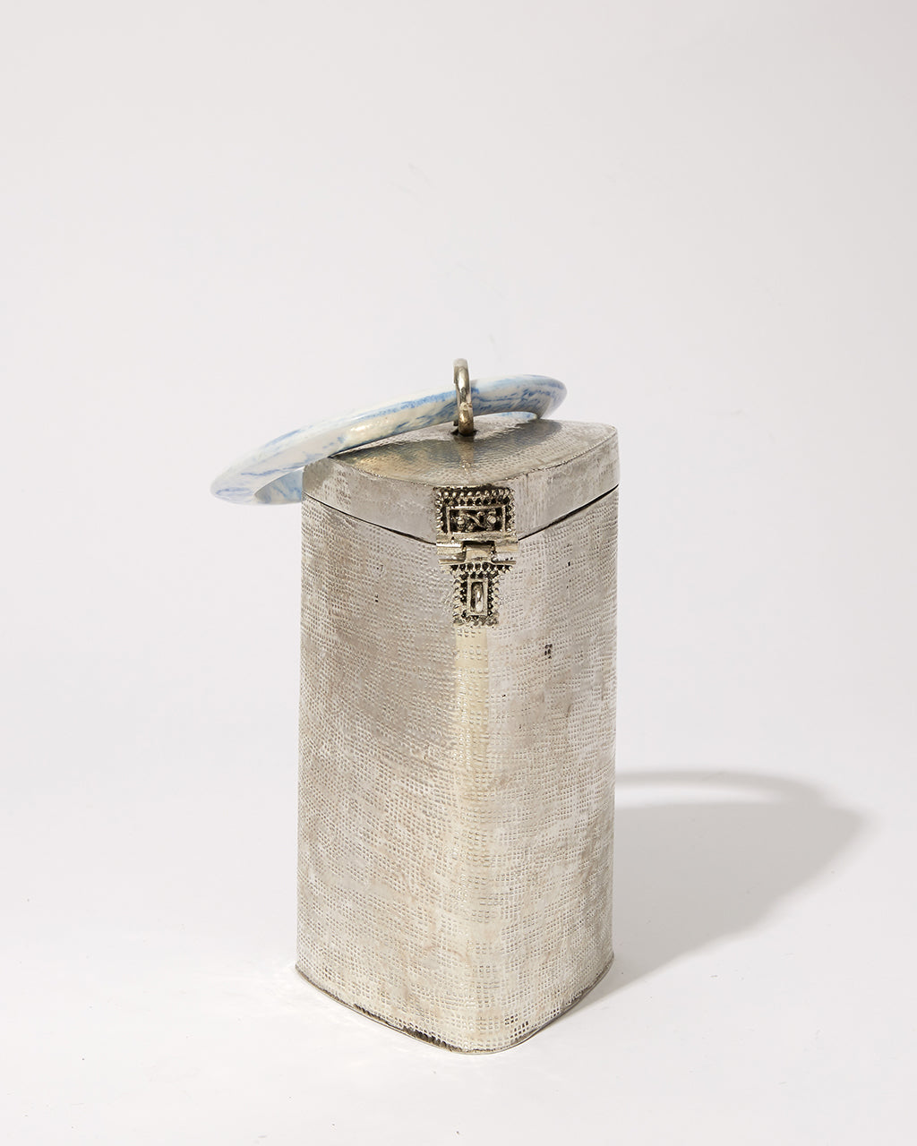 Three-quarter studio view of the Right Off The Edge brass handbag, featuring a unique triangular cylinder shape and blue marble resin handle.