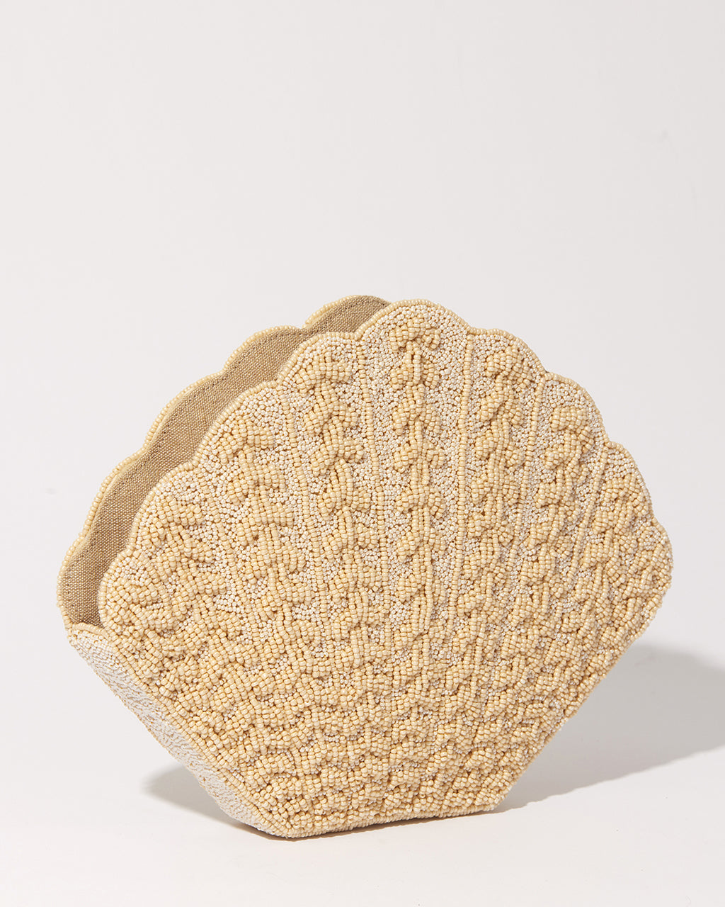 Three-quarter studio view of the Stand Still champagne beaded clutch featuring a sculptural shell-shaped silhouette and embossed beadwork.