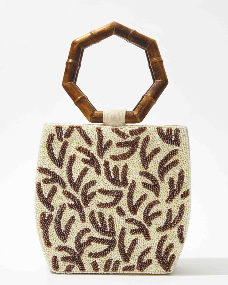 Three-quarter studio view of the Symbolic Path beaded bag featuring white glass beads, a brown embossed leaf pattern, and curved bamboo handles.
