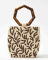 Three-quarter studio view of the Symbolic Path beaded bag featuring white glass beads, a brown embossed leaf pattern, and curved bamboo handles.