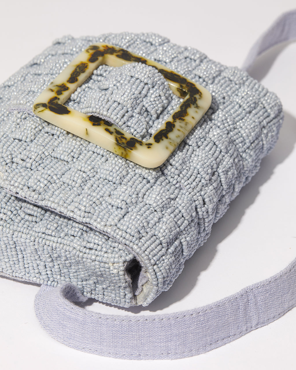 Three-quarter view of the artisan-made Uncovered Layers waist bag in soft blue featuring a hand-beaded woven pattern and resin buckle.
